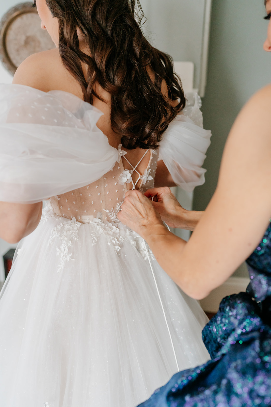 a getting ready wedding picture of the bridesmaid helping the bride tying the wedding dress