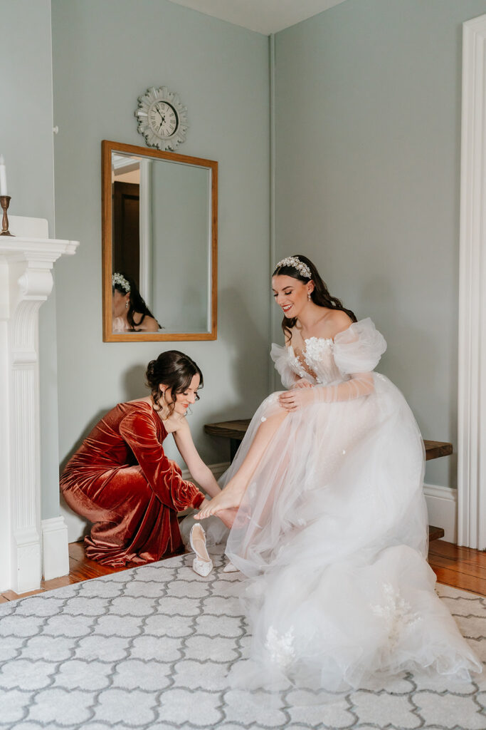 candid wedding photo of the bridesmaid helping the bride put on her shoe