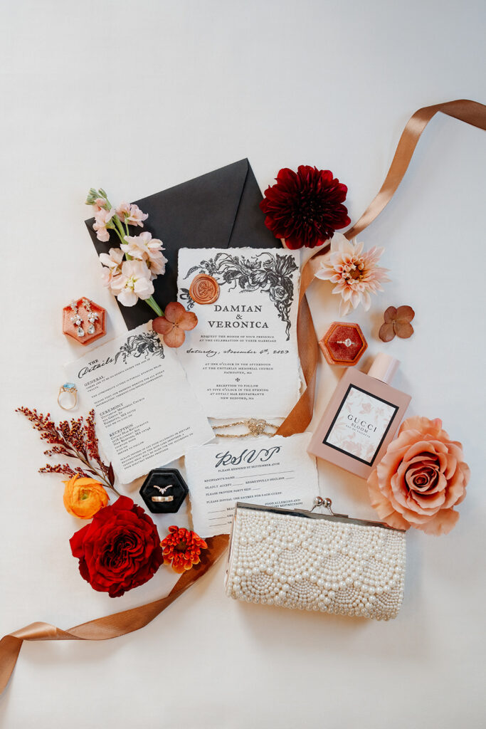 Orange theme flat flay of full wedding invitation suite, RSVP, wedding menu and wedding invitation. The bride's ring, perfume, earrings and pearl clutch