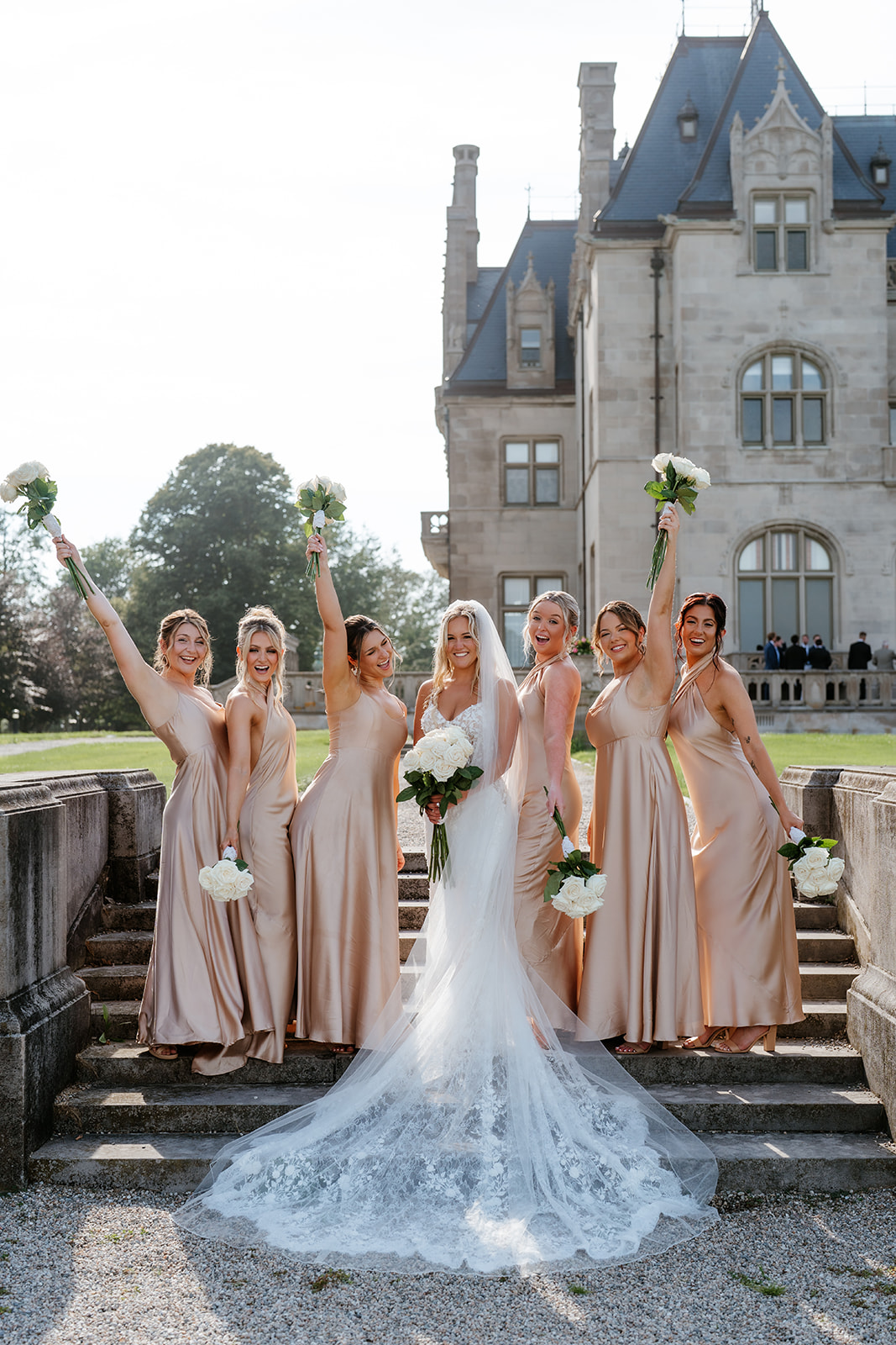 bride and bridesmaids wearing champagne dresses with their bouquet up in the air at Ochre Court 