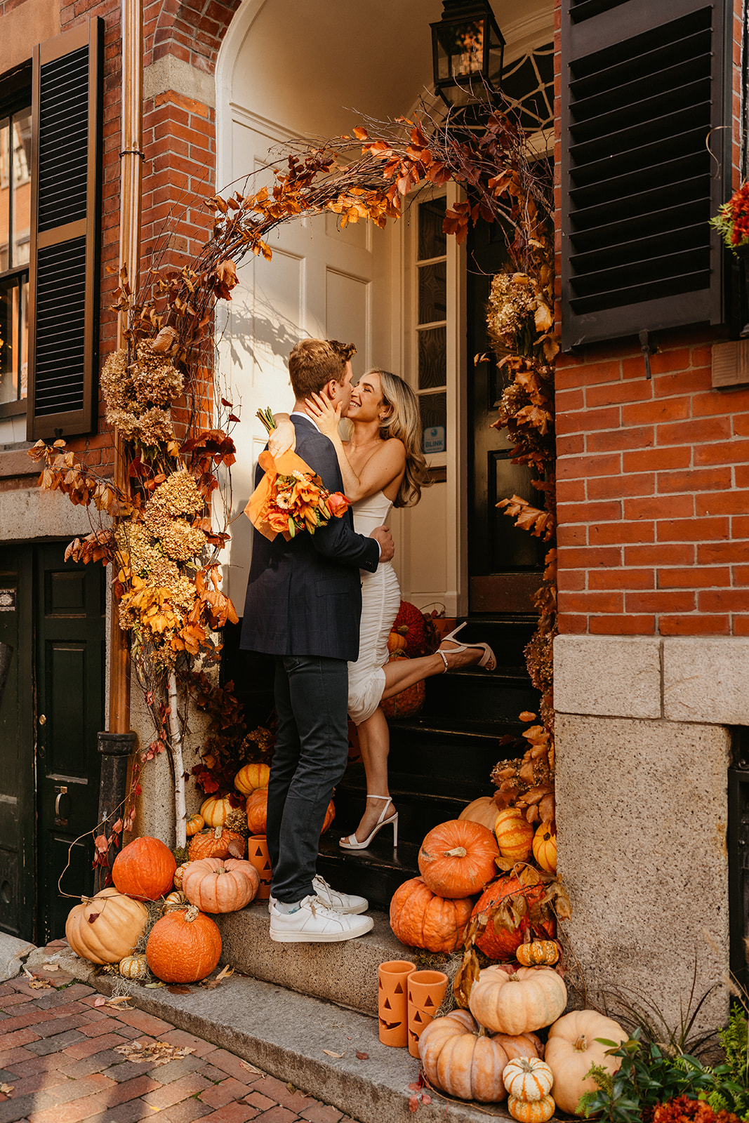 the engaged couple stands in front of a building with pumpkins for fall engagement photos