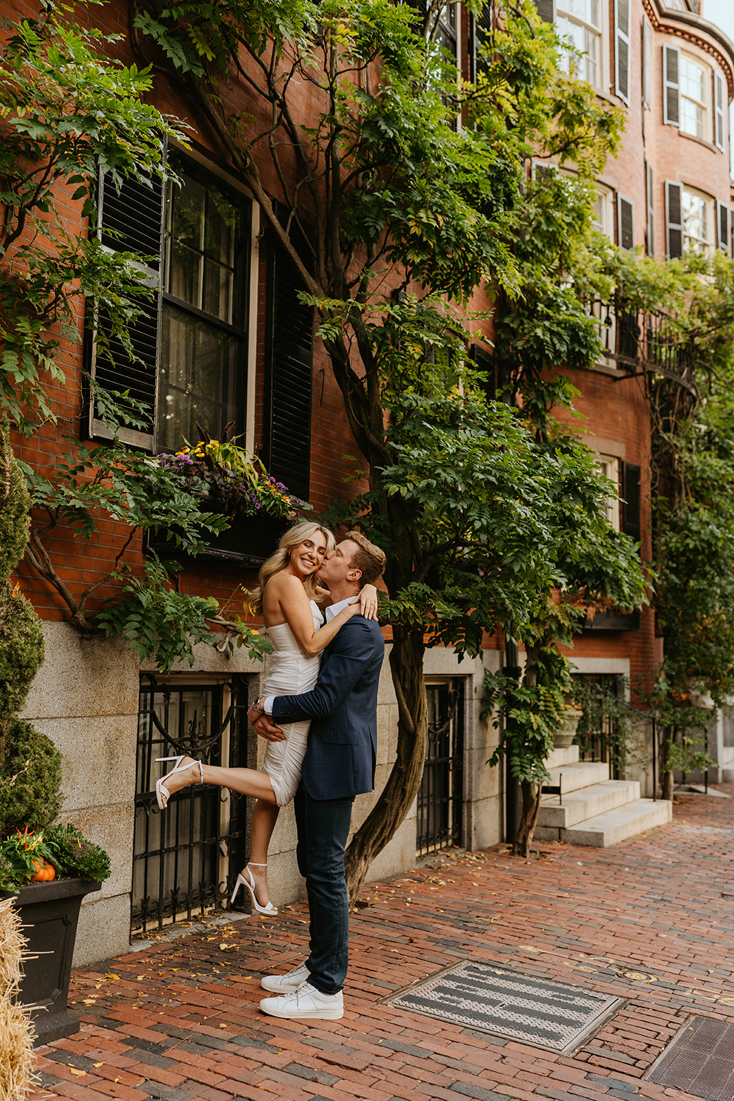 a man carries his future bride while kissing her cheek outdoor in Boston