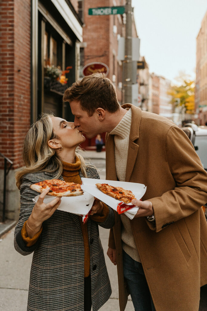 engaged couple kissing and holding pizza for their fall engagement shoot