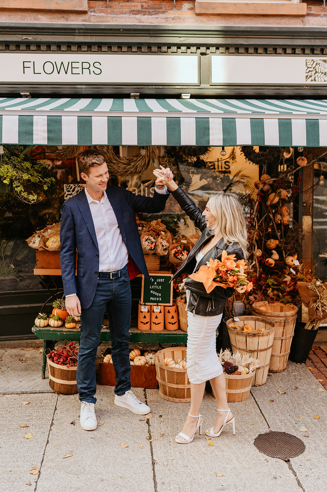 engaged couple holding hands in front of a florist shop with autumn decor