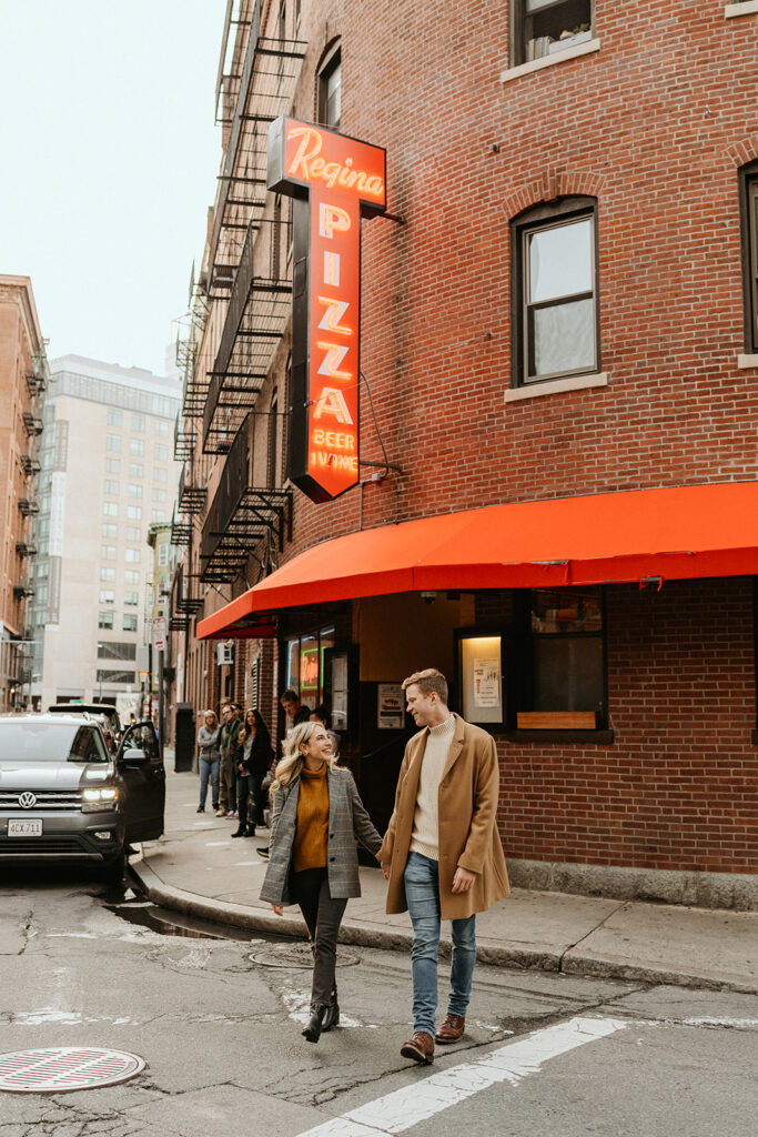 engaged couple holding hands and walking in North End with warm, fall clothes 