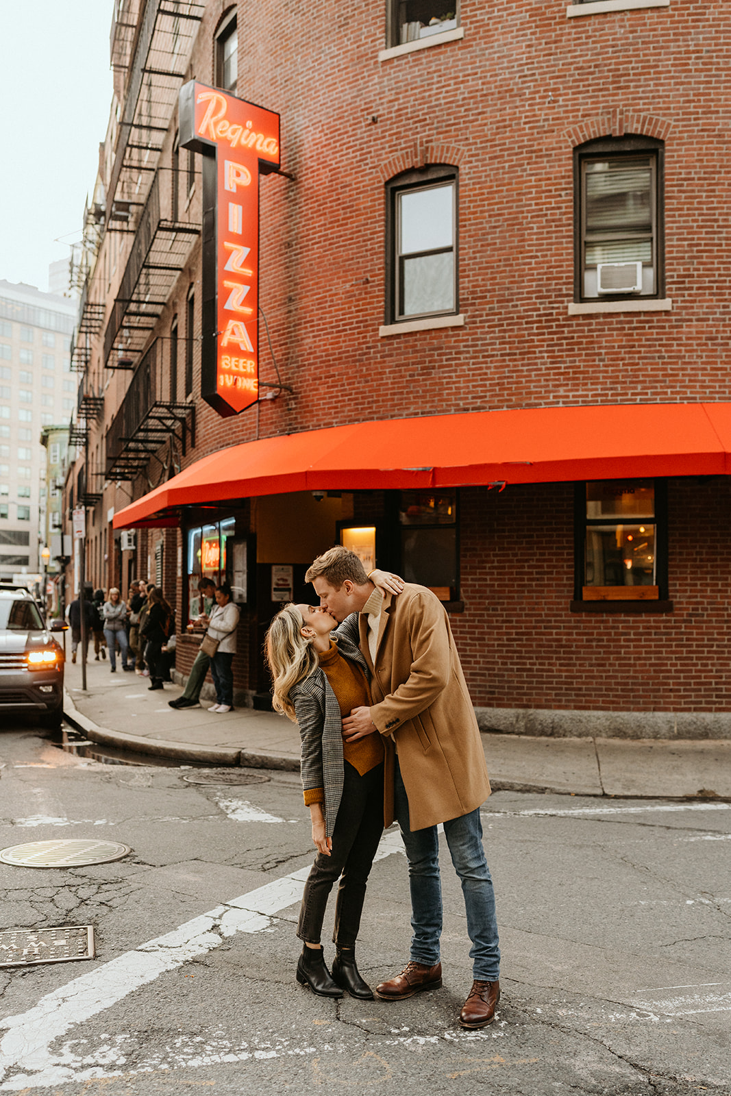 engaged couple kissing in the streets near a pizza place in Boston