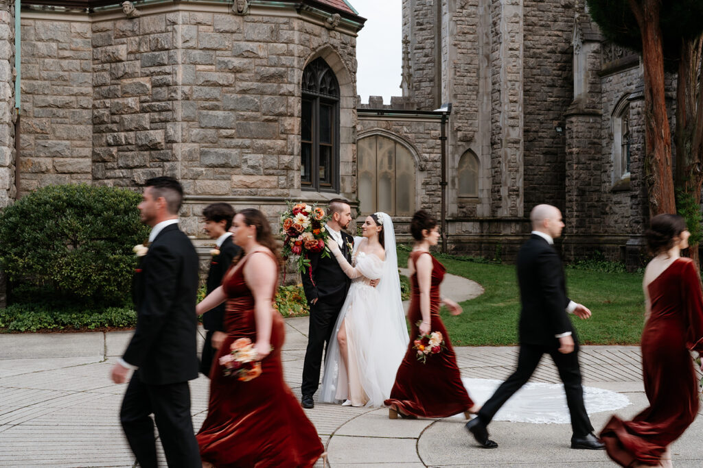 modern wedding photo of bride and groom while bridesmaids and groomsmen walking through