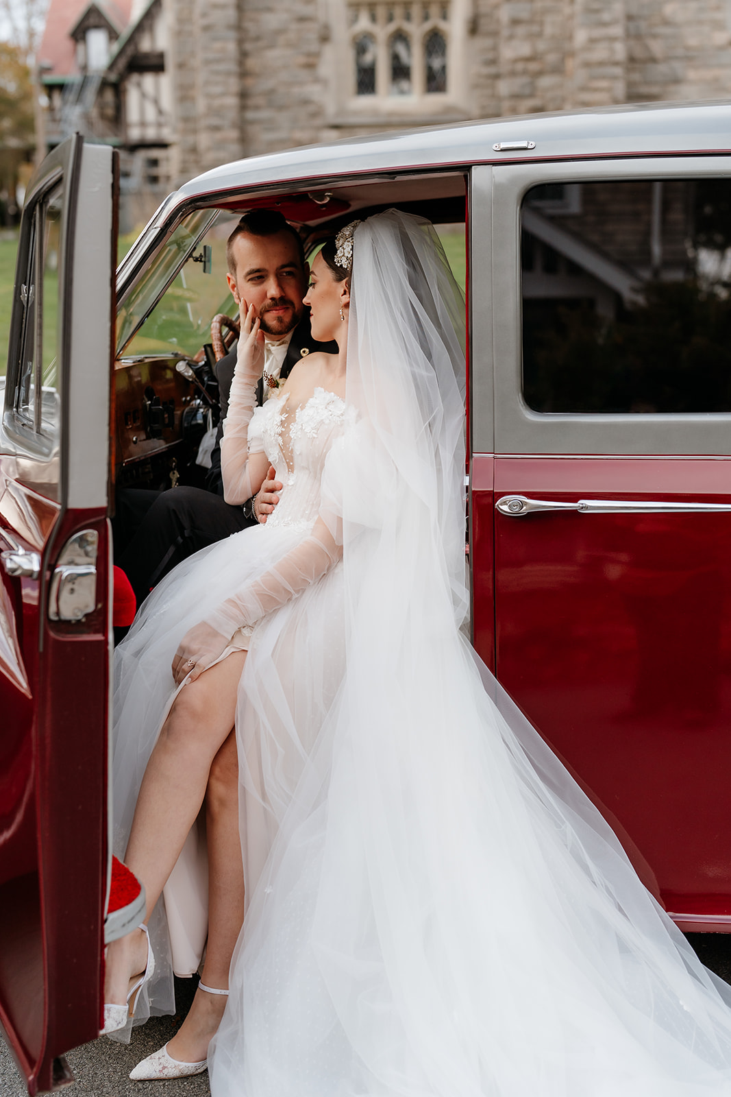 bride and groom looking at each other before stepping out of their vintage red car for their wedding reception