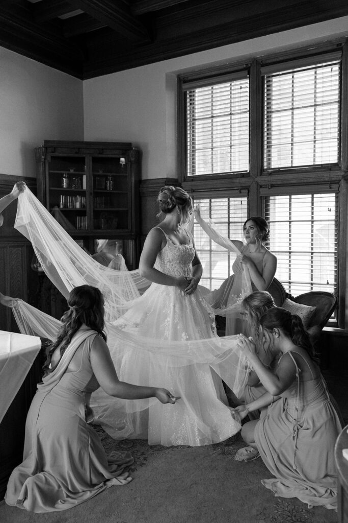 timeless wedding photo of bride getting ready with the help of her bridesmaids