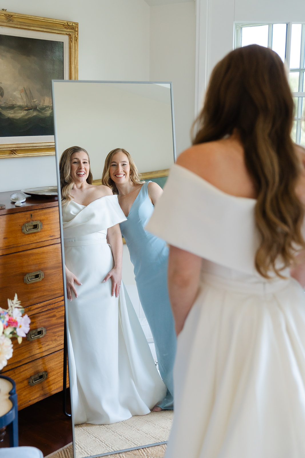 bride and her bridesmaid looking at the mirror smiling while getting ready