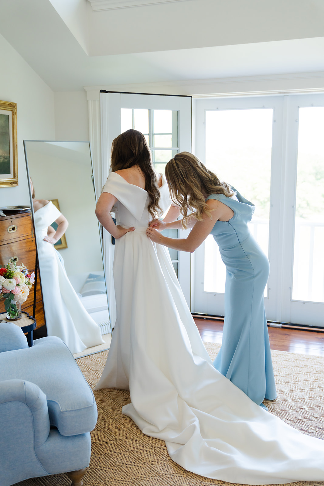 bridesmaid helping the bride putting on her wedding dress