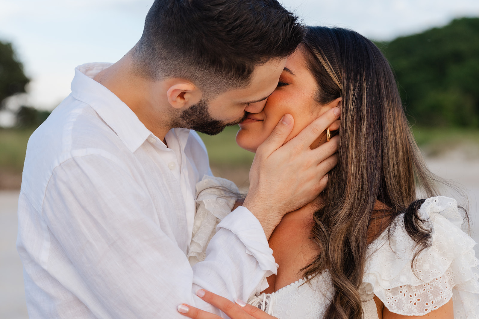 A close-up of the couple sharing an intimate kiss on the beach at sunset, with the soft lighting and tranquil water setting the mood for a memorable Cape Cod engagement photo.