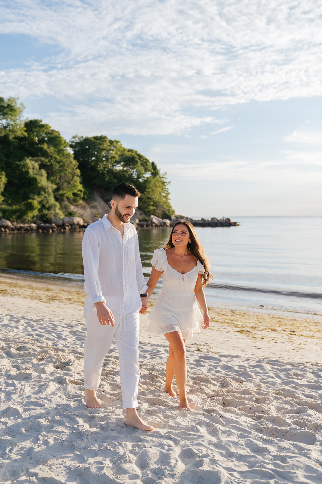 A couple walking hand-in-hand on Old Silver Beach in Falmouth, with the sun setting over the water, creating a dreamy golden hour glow. A perfect example of Cape Cod Engagement Photos.