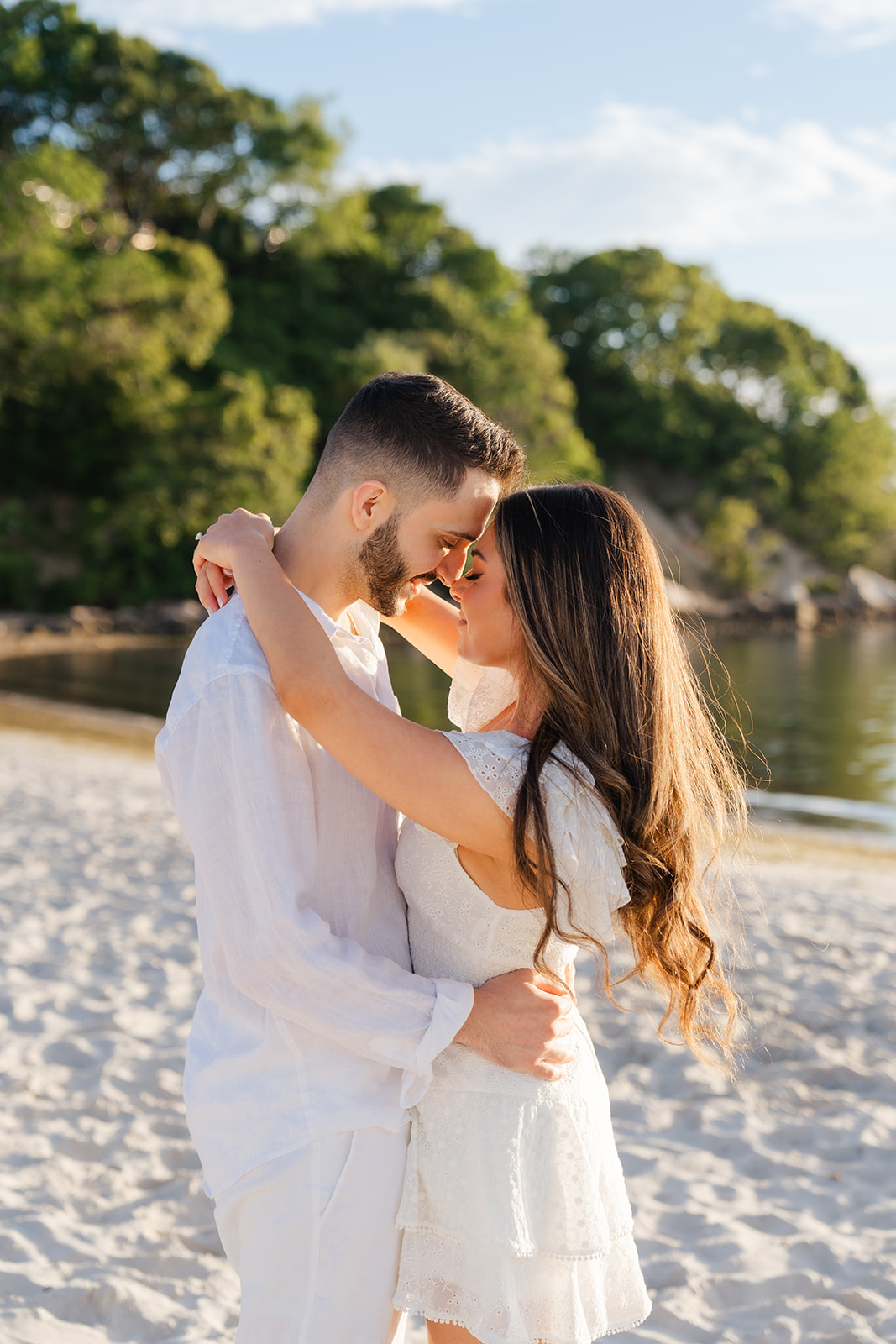 The couple embracing on the sand, laughing and enjoying each other’s company as the sun begins to set over the Cape Cod horizon, creating beautiful engagement photos.