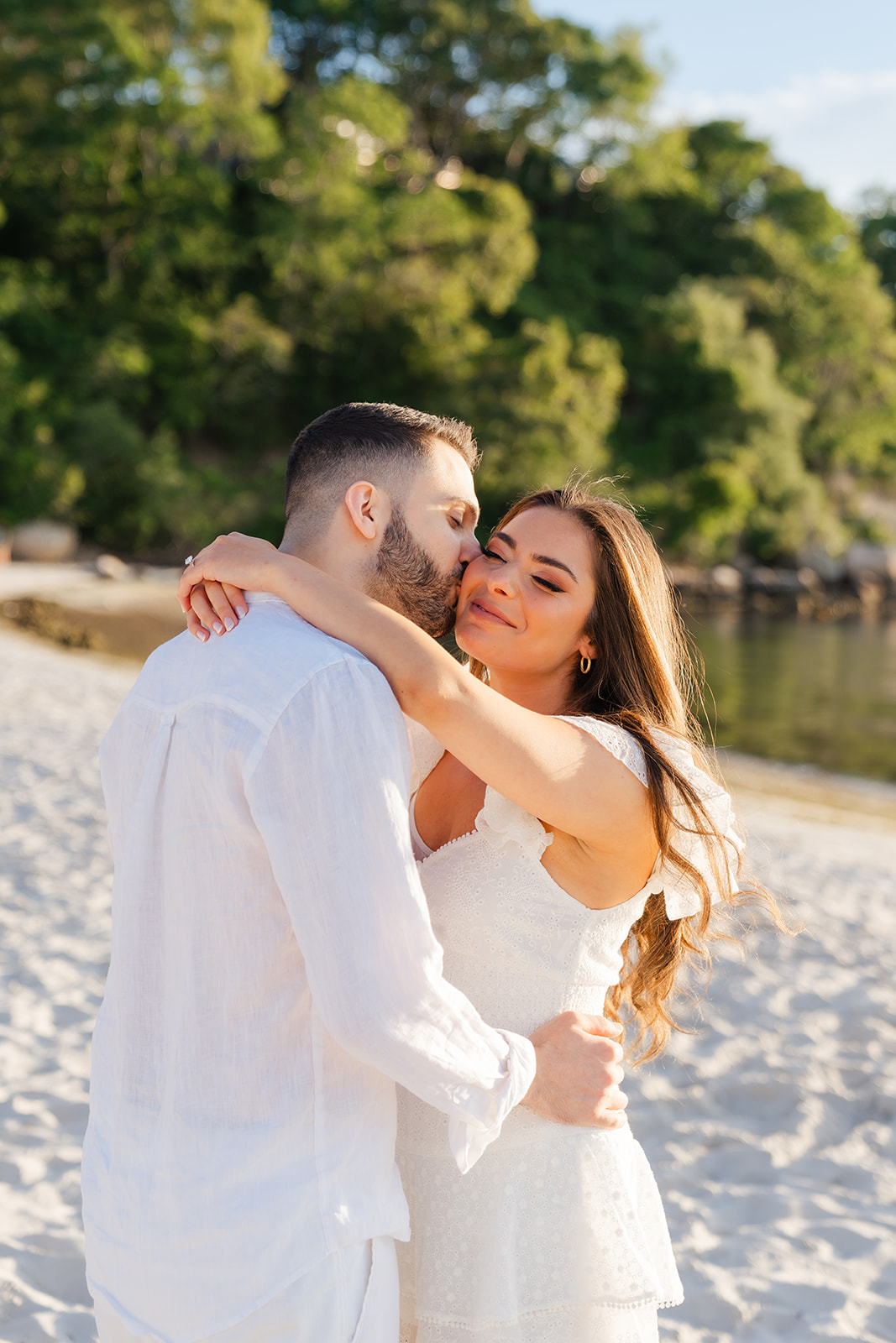 The couple embracing on the sand, laughing and enjoying each other’s company as the sun begins to set over the Cape Cod horizon, creating beautiful engagement photos.