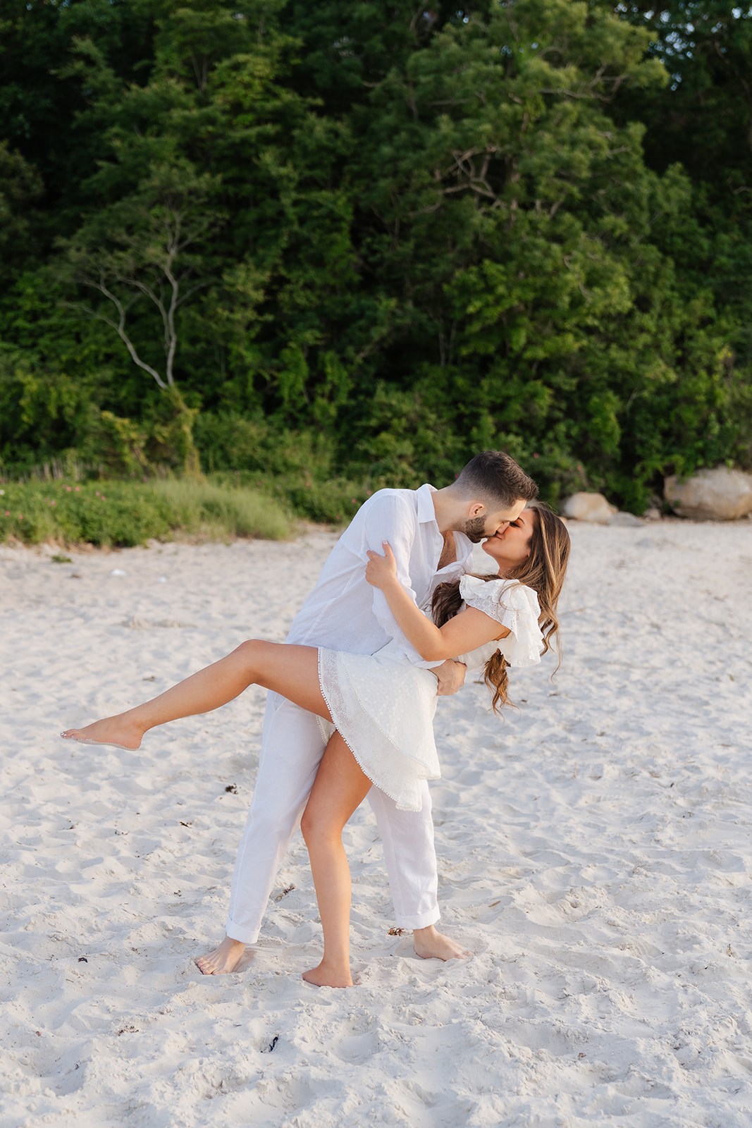 A couple sharing a sweet kiss on the beach at Old Silver Beach in Falmouth, with the soft golden hour lighting creating a romantic vibe in this Cape Cod engagement photo.