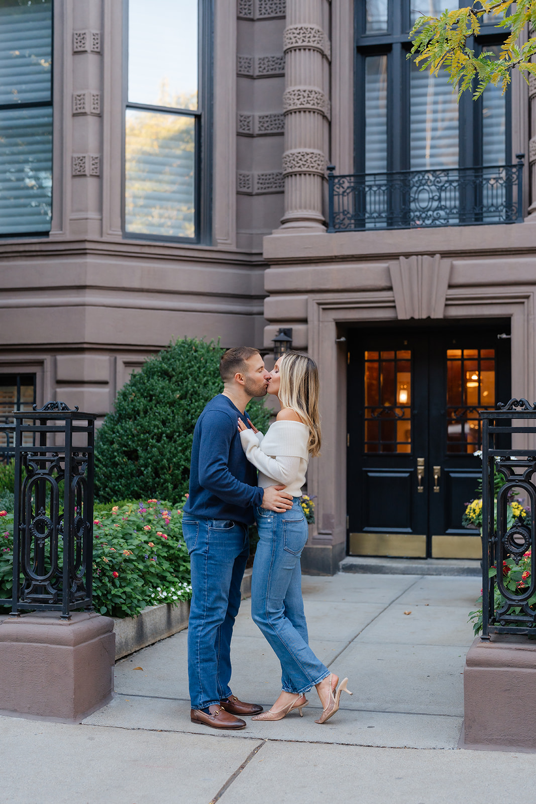 Engaged couple sharing a kiss near the garden fence with the Boston skyline peeking through the greenery in the background.