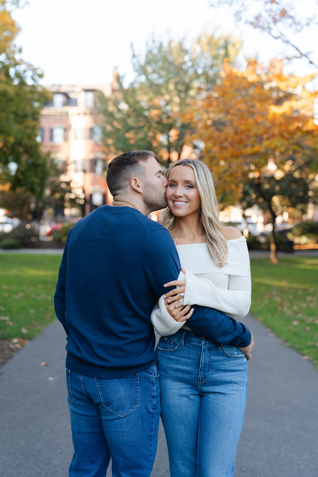 Couple laughing and holding hands while walking down a garden path in the Boston Public Garden, with beautiful autumn foliage in the background.