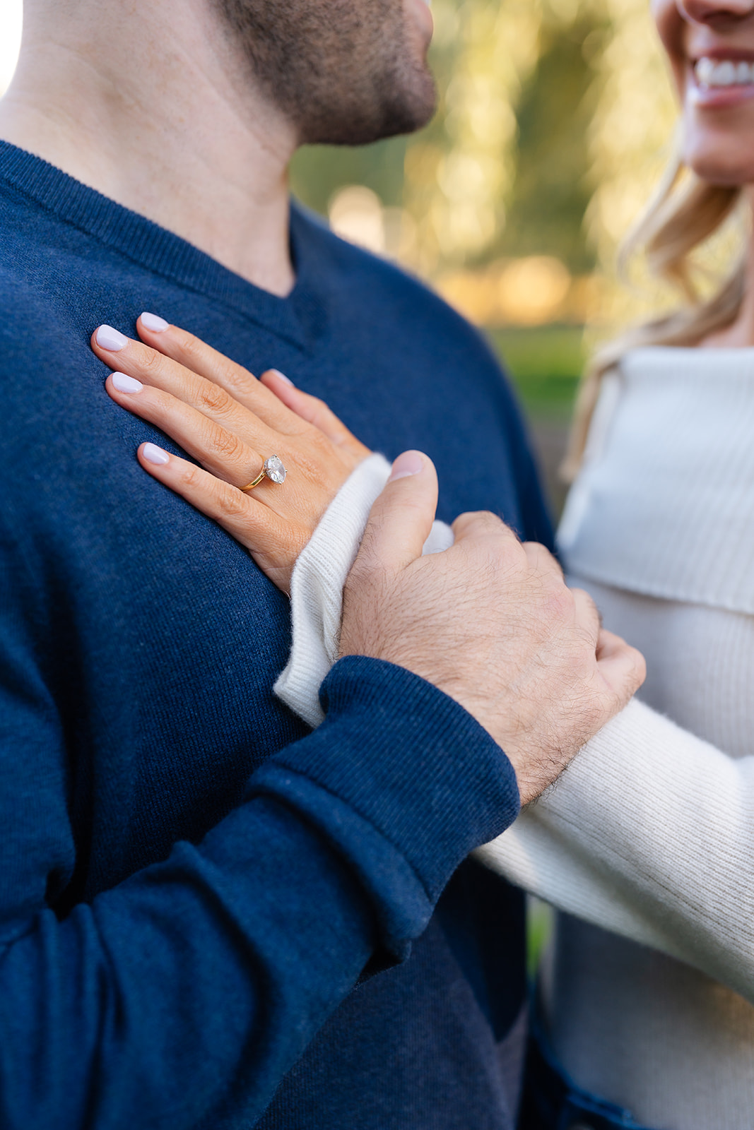 Close-up of a couple’s hands intertwined, showcasing the engagement ring while holding each other in the Boston Public Garden, a serene setting for engagement photos.