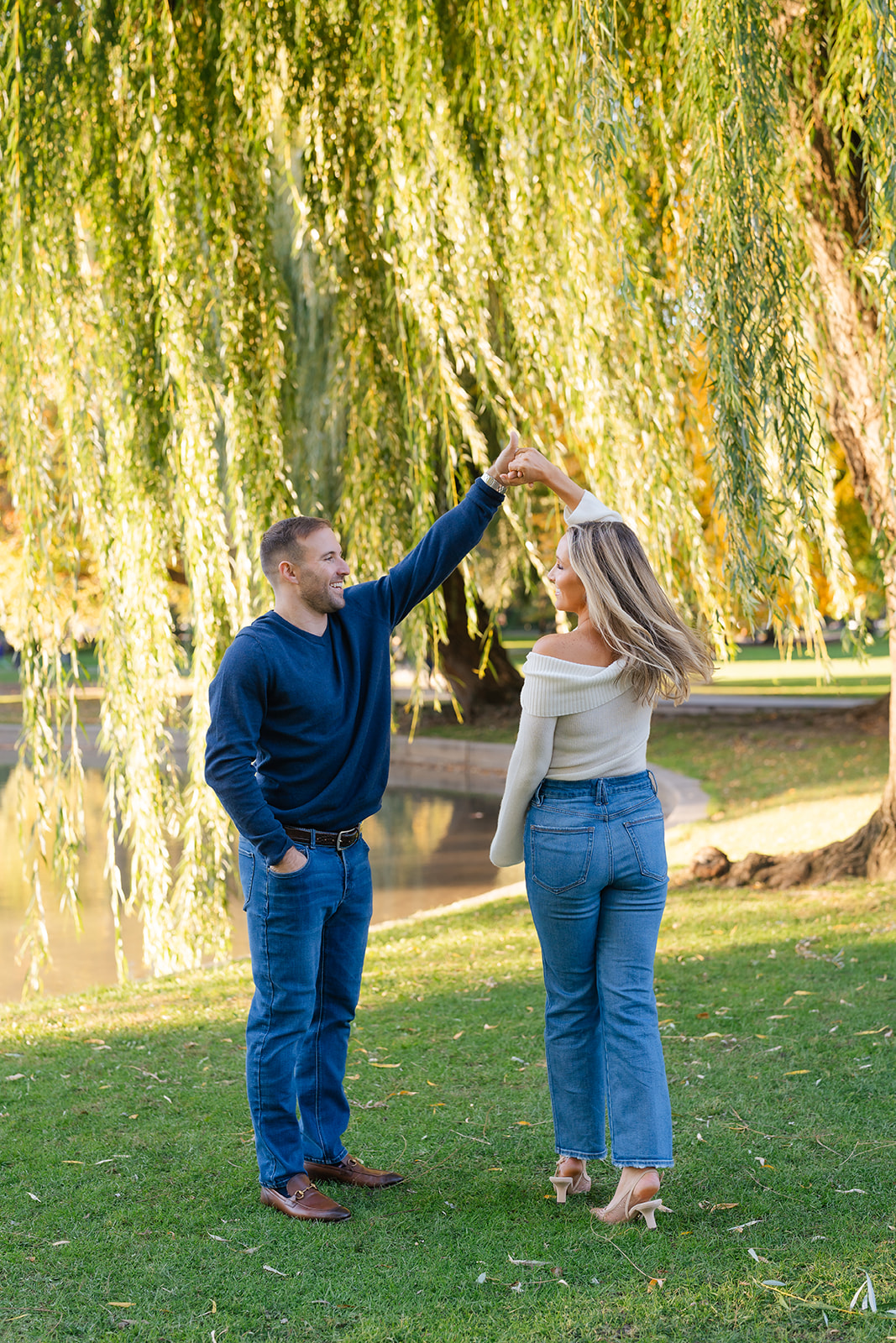 Couple dancing together near the bridge in the Boston Public Garden, surrounded by lush greenery.