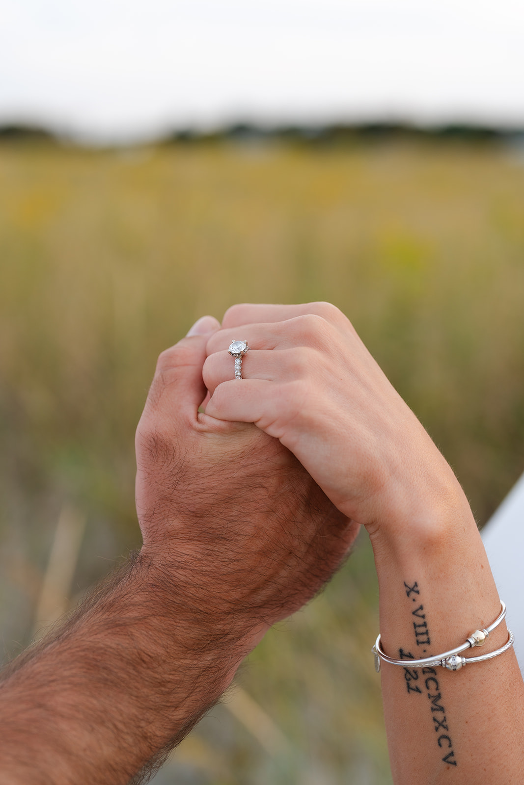 Close-up of a couple holding hands with an engagement ring visible during a beach engagement session at sunset.