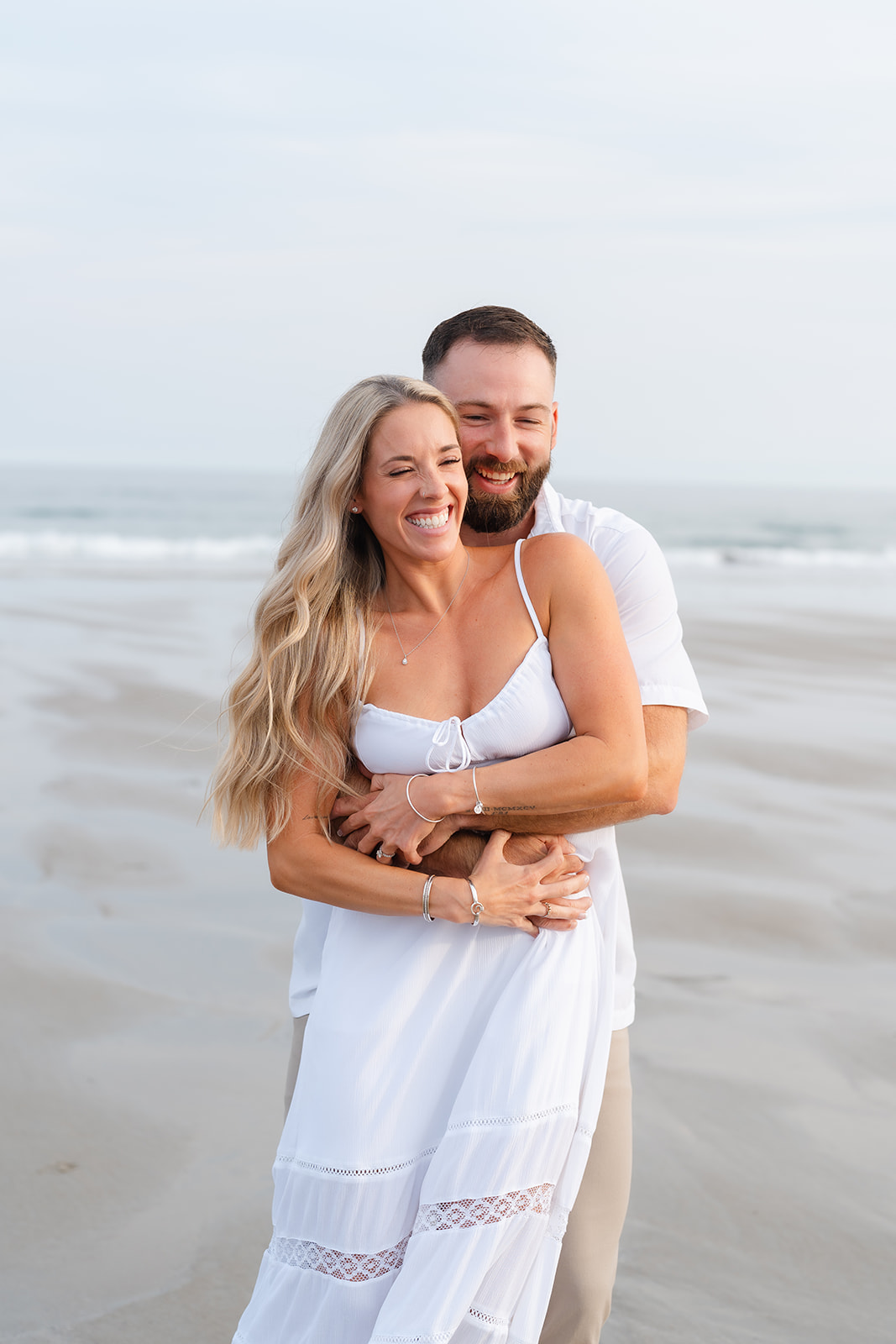 A tender moment as a couple embraces each other on the beach, their smiles showing the deep connection and happiness during their Beach Engagement session.