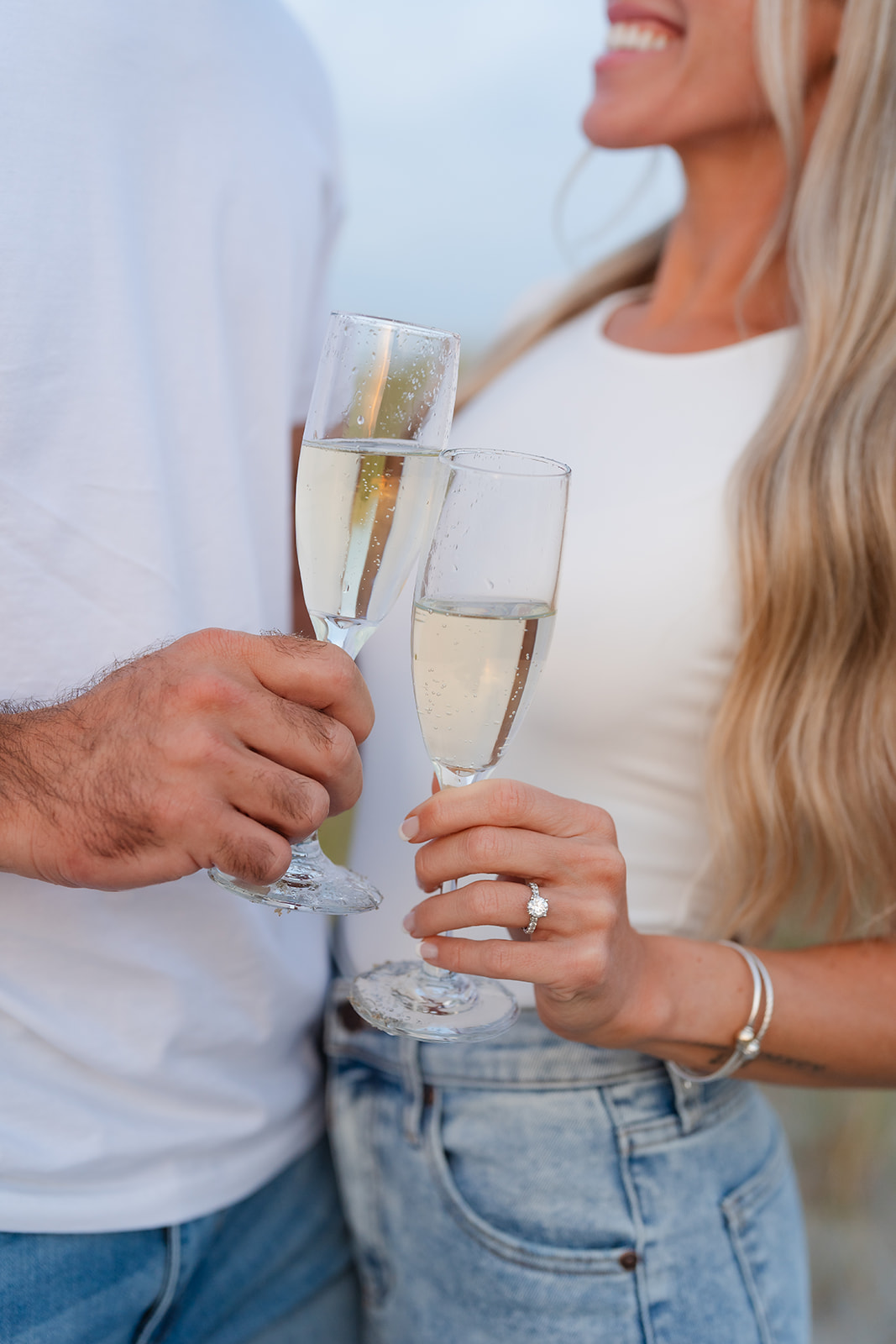 Fun and candid moment captured during a beach engagement session with a couple laughing while popping champagne on the beach.