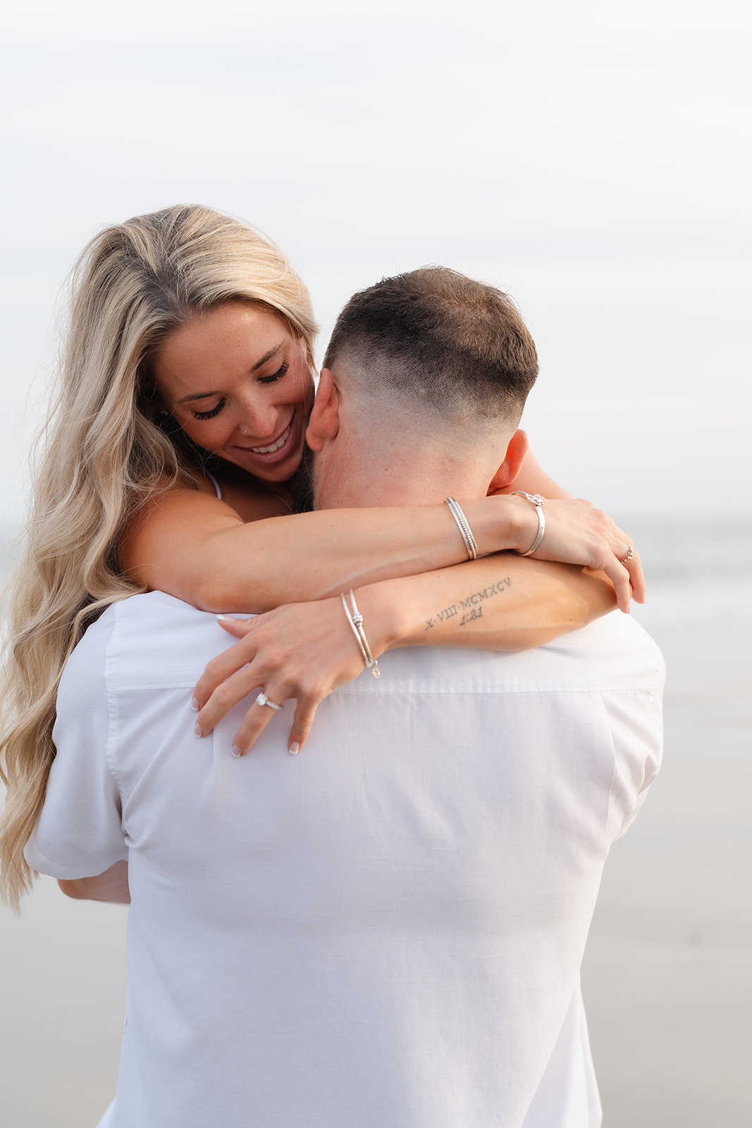 A tender moment as a couple embraces each other on the beach, their smiles showing the deep connection and happiness during their Beach Engagement session.