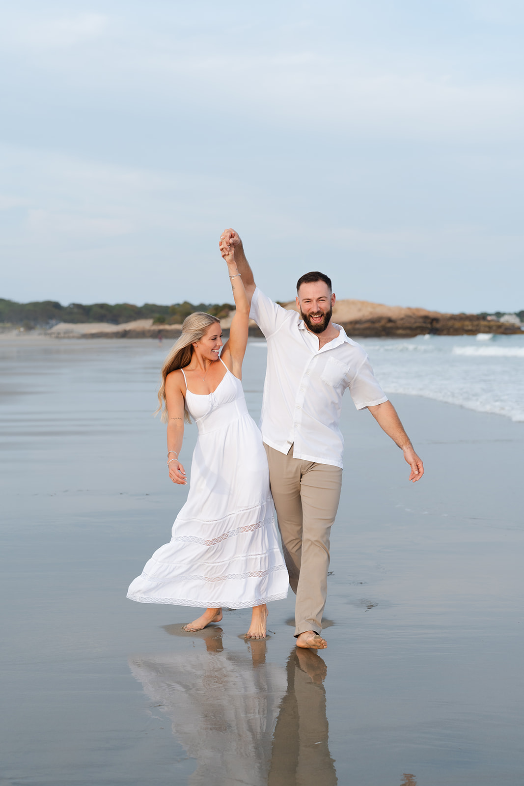 A couple twirling and dancing together barefoot on the beach, full of laughter and love during their Beach Engagement session.