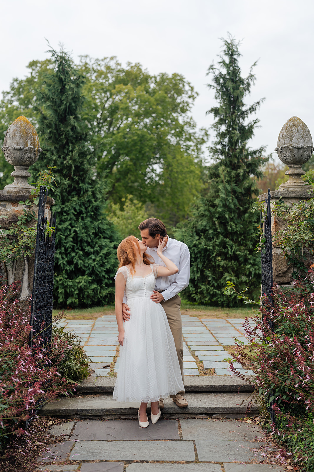 Engaged couple standing close, surrounded by blooming flowers in a picturesque garden, showcasing their love and unique engagement shoot ideas at Stevens-Coolidge House & Gardens.