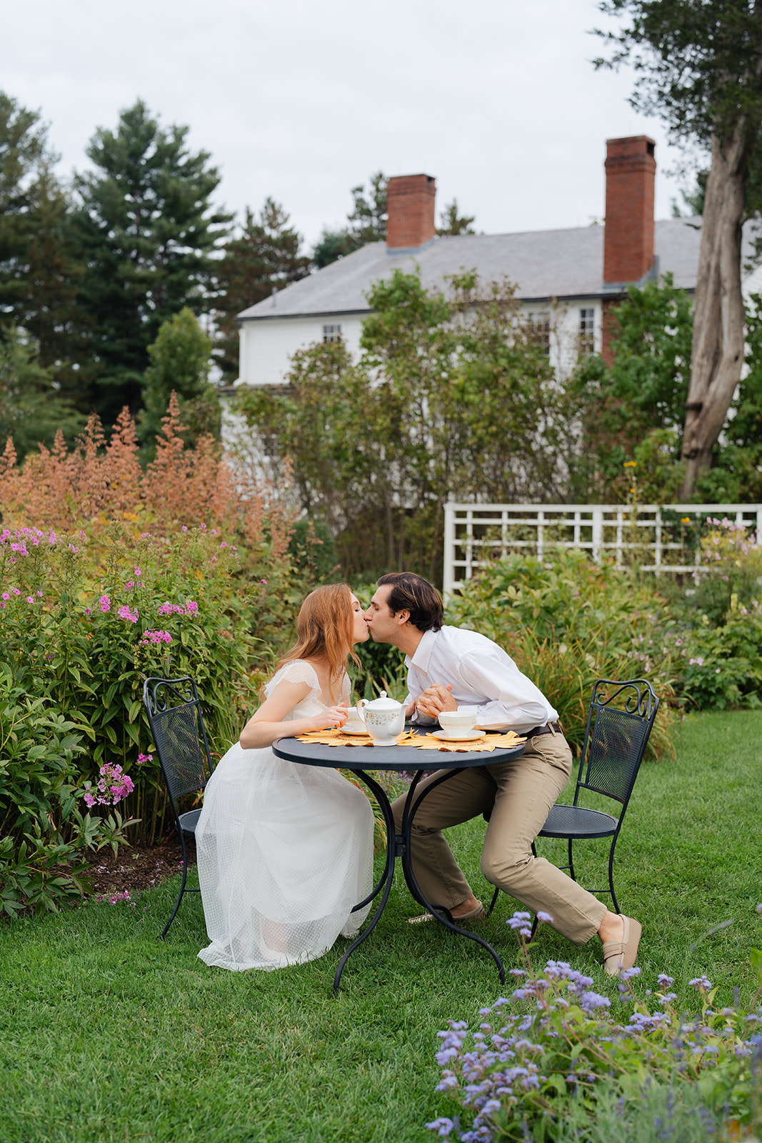 A couple sharing a sweet kiss over a tea set at Stevens-Coolidge House & Gardens, showcasing unique engagement shoot ideas that tell their love story.