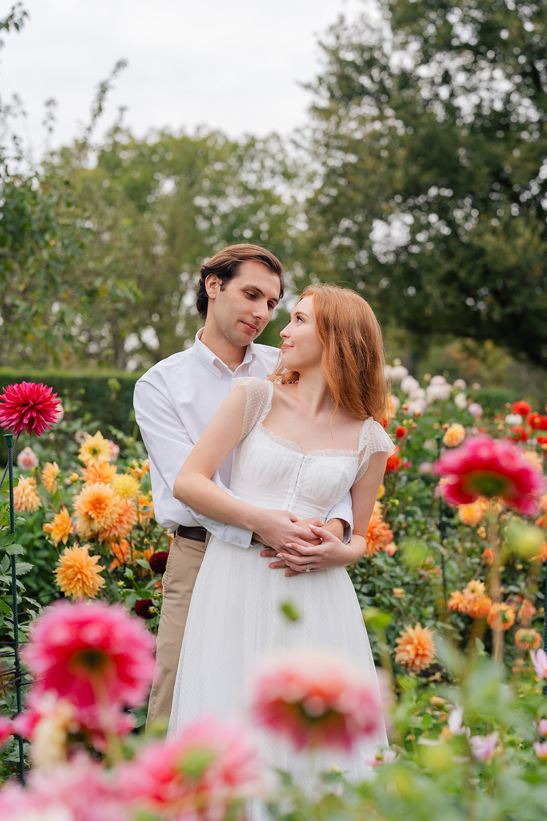 Engaged couple standing close, surrounded by blooming flowers in a picturesque garden, showcasing their love and unique engagement shoot ideas at Stevens-Coolidge House & Gardens.