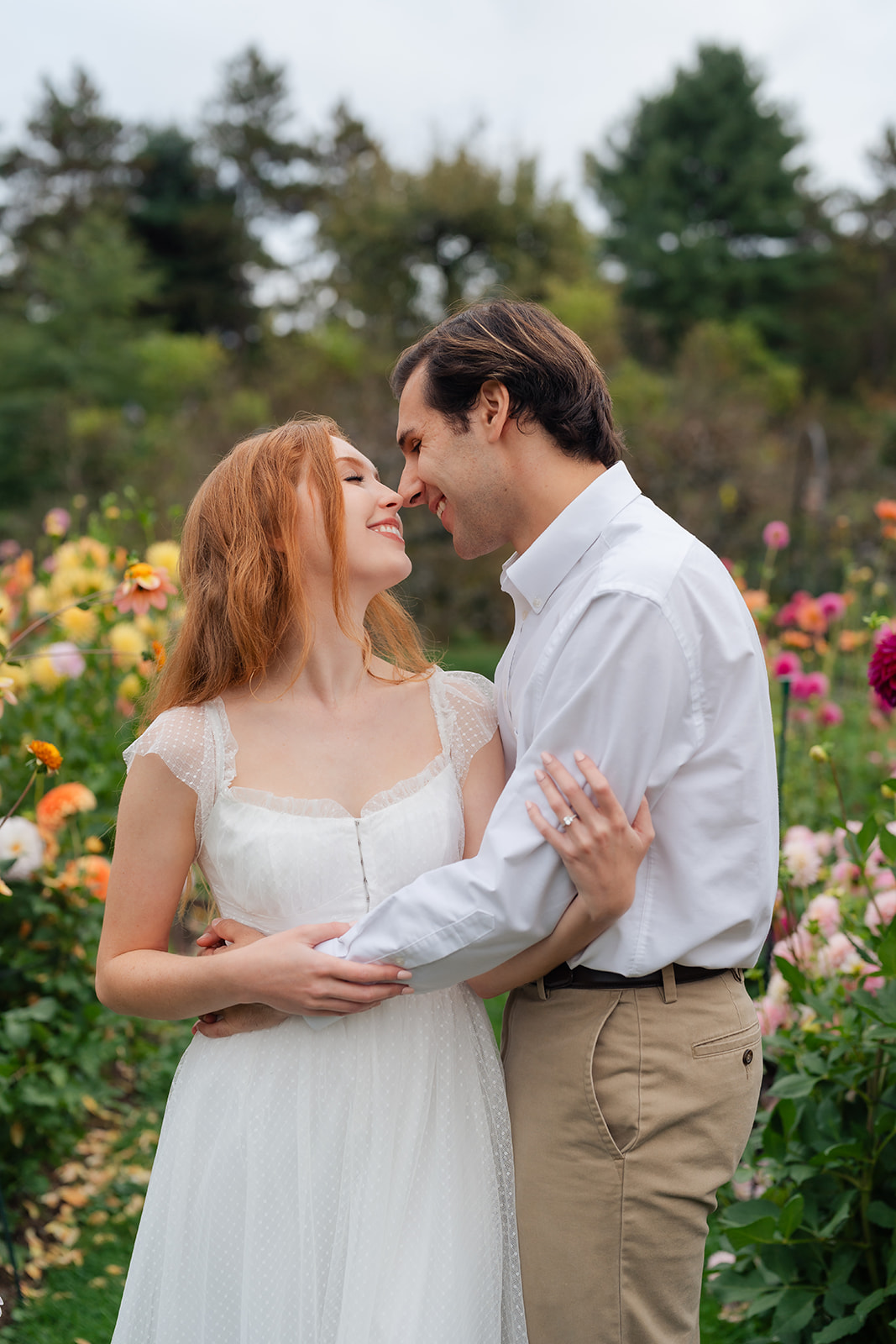 Engaged couple standing close, surrounded by blooming flowers in a picturesque garden, showcasing their love and unique engagement shoot ideas at Stevens-Coolidge House & Gardens.