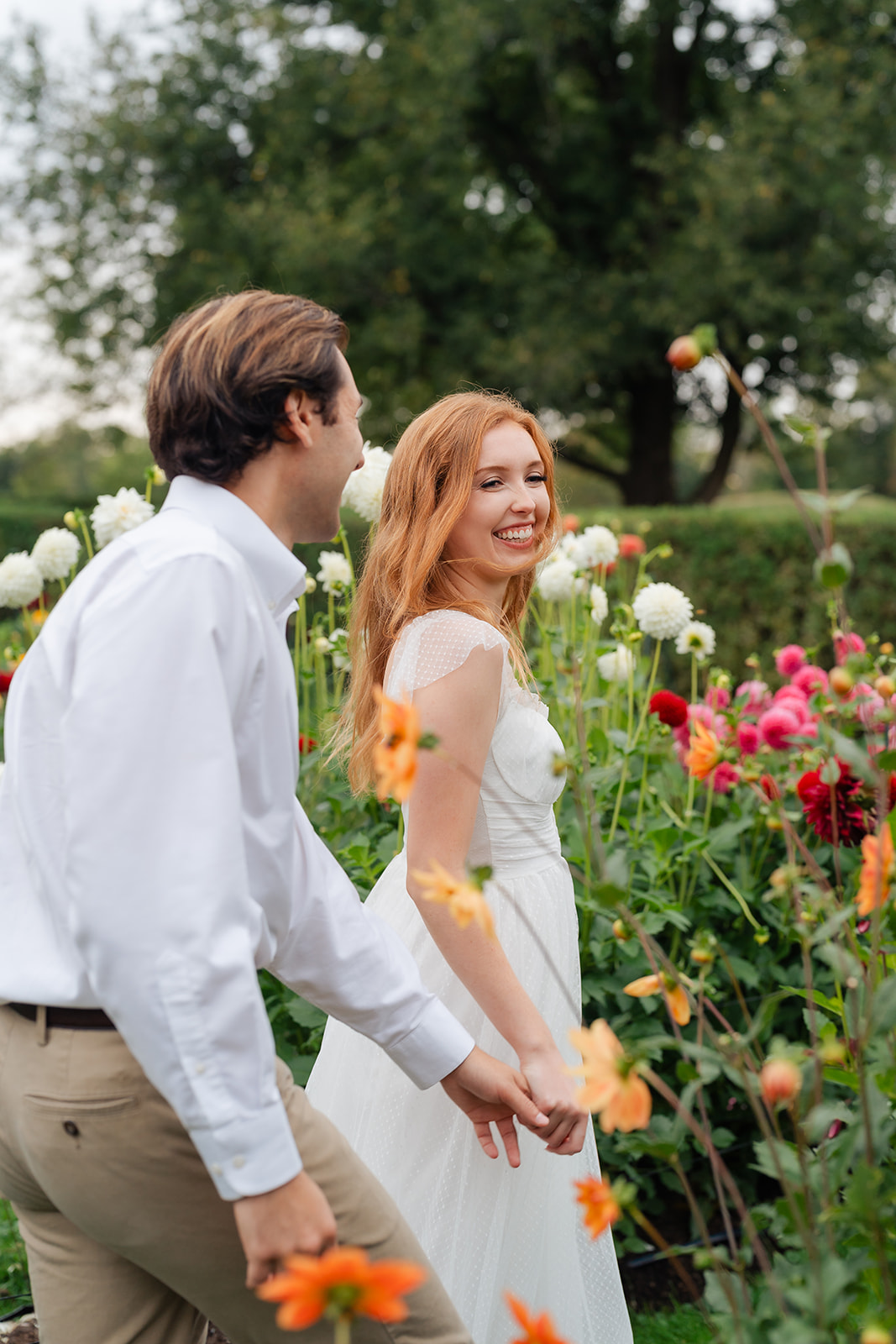 The couple walking side by side, both smiling joyfully, amidst a vibrant garden of flowers. This candid moment perfectly captures their love and excitement, making it a memorable part of their engagement session.