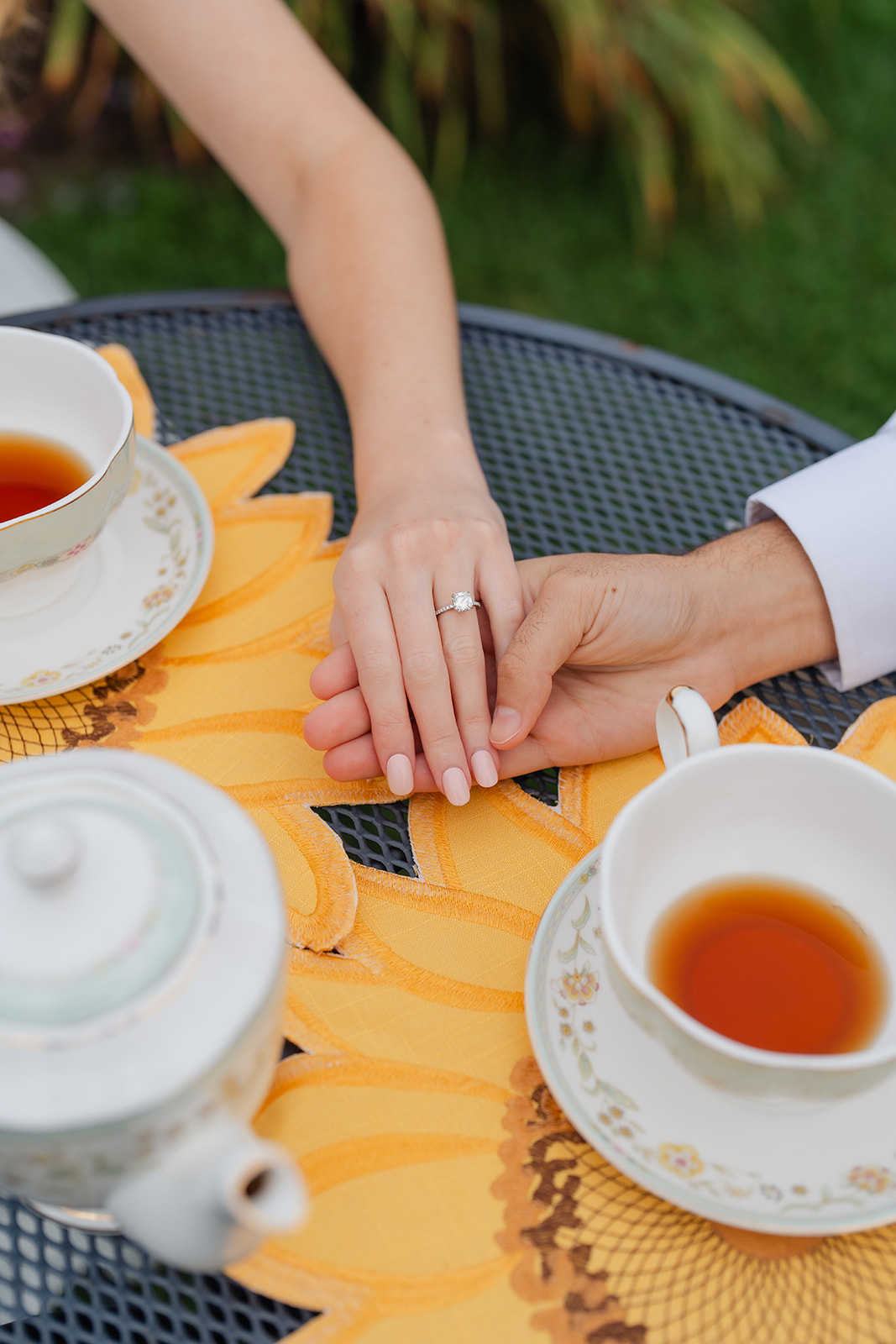 A couple holding hands, with a beautifully captured shot of their engagement rings and cups of tea, adding a personal touch to their engagement session.