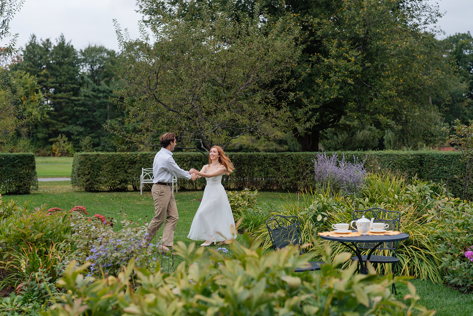 The couple dancing joyfully in a lush garden filled with greenery, showing how unique engagement shoot ideas like incorporating movement and interaction can create dynamic, beautiful photographs that truly tell the story of the couple’s relationship.