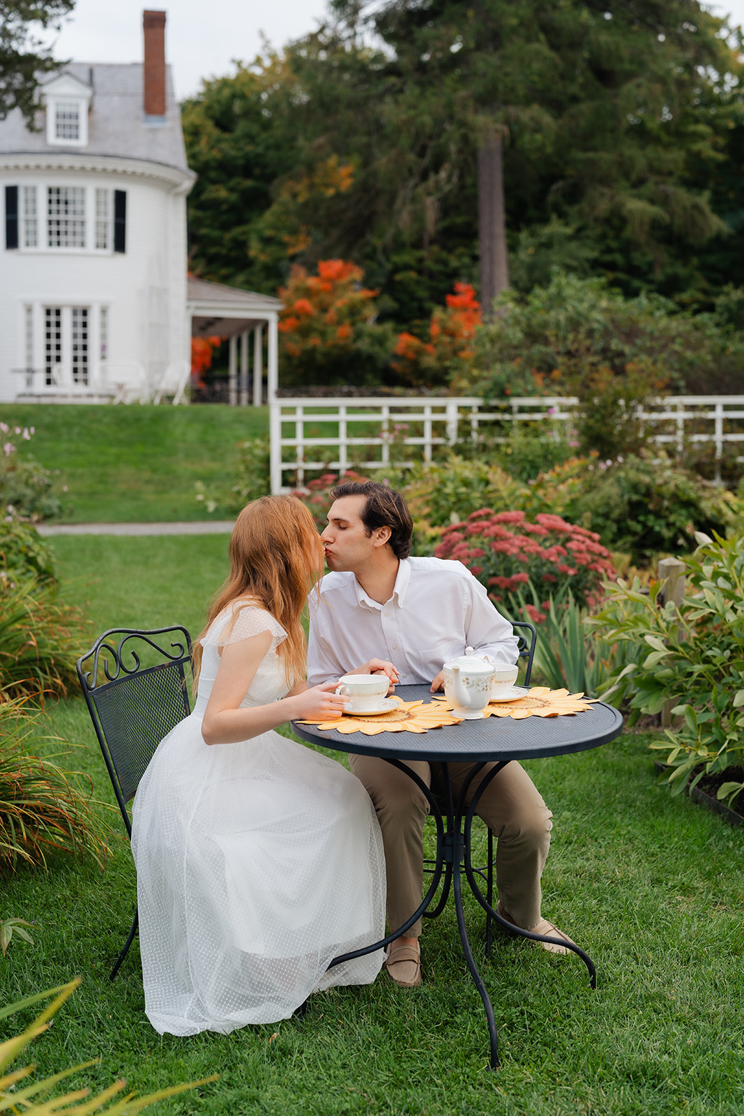 A romantic kiss between a couple at their engagement session, surrounded by lush gardens and tea cups—unique engagement shoot ideas come to life.