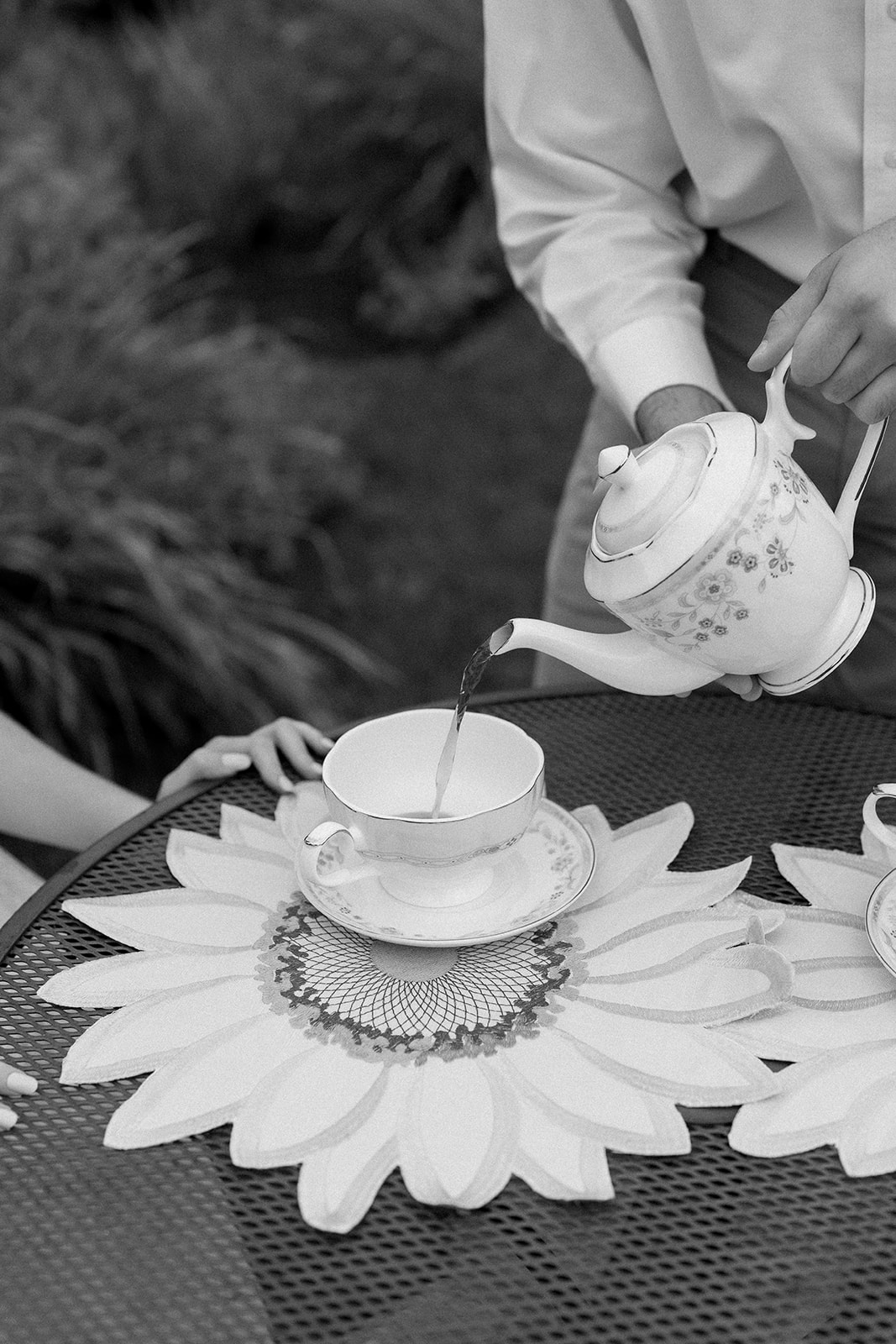 A close-up shot of a man pouring tea for his fiance during their creative engagement shoot, capturing a unique and intimate moment with a vintage vibe.